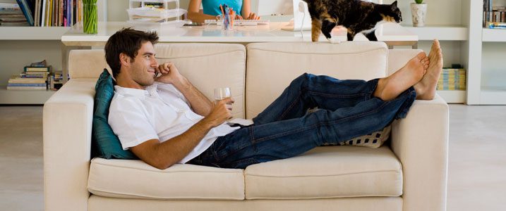 A man is sitting on the couch drinking wine