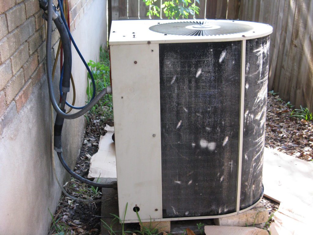 A dirty air conditioner unit sitting outside of the house.