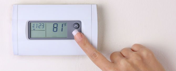 A person is adjusting the temperature on an electronic thermostat.