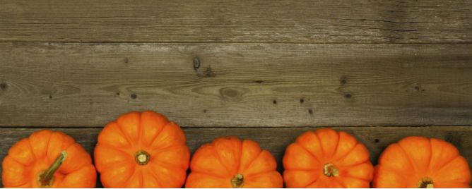 Three pumpkins sitting on top of a wooden table.