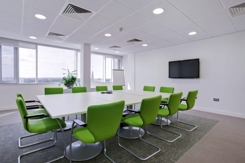A conference room with green chairs and white tables.